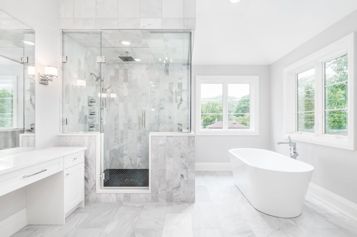A large luxurious marble bathroom with a standalone tub, white vanity, and glass shower with marble tiles