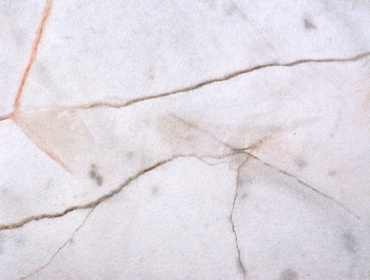 Gray marble, polished natural stone surface with deep black and orange cracks throughout the material, close-up. Seamless background texture.