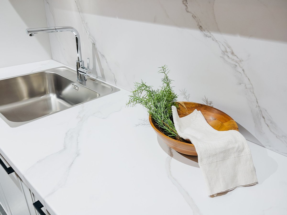 Modern kitchen counter with marble texture, stainless sink, chrome faucet, rosemary in wood bowl